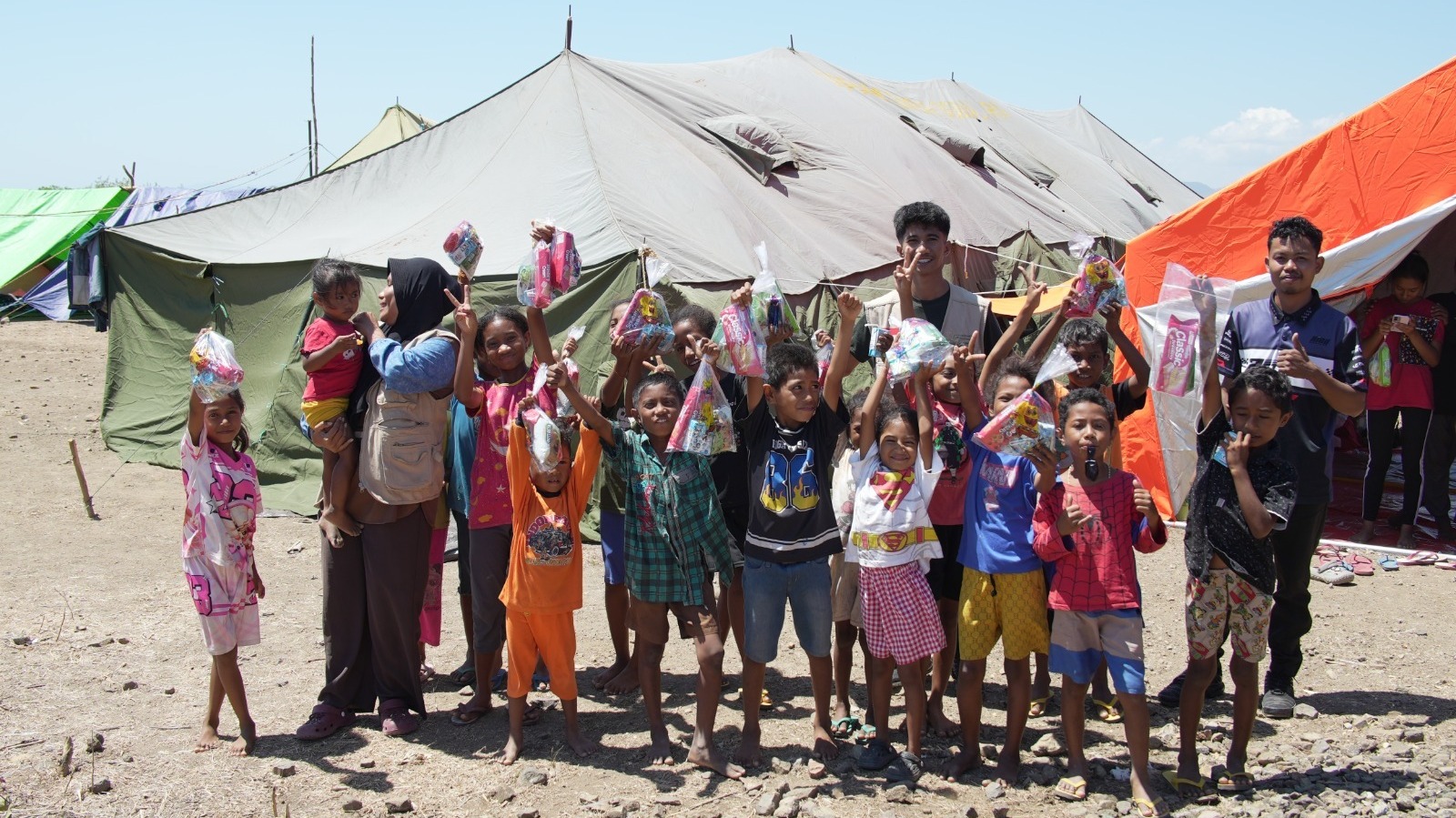 penyertaan-bantuan-anak-anak-di-pengungsian Foto bersama relawan dan anak-anak penyintas bencana di depan tenda pengungsian setelah penyaluran bantuan.