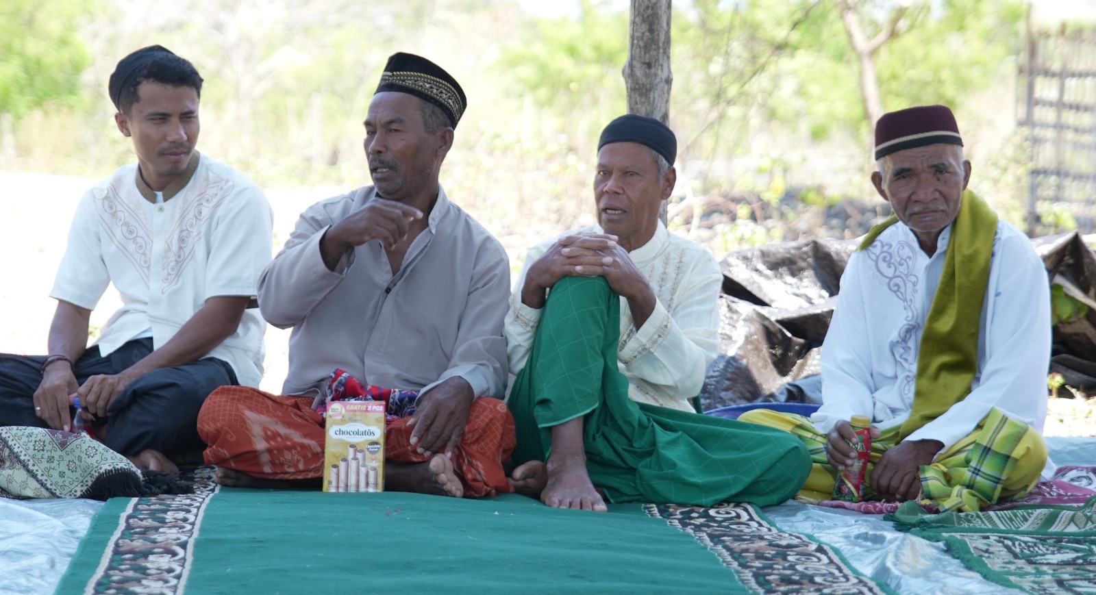 Empat tokoh masyarakat atau pemuka agama Desa Waekokak duduk bersama di atas tikar darurat, berdiskusi di lokasi pengungsian.