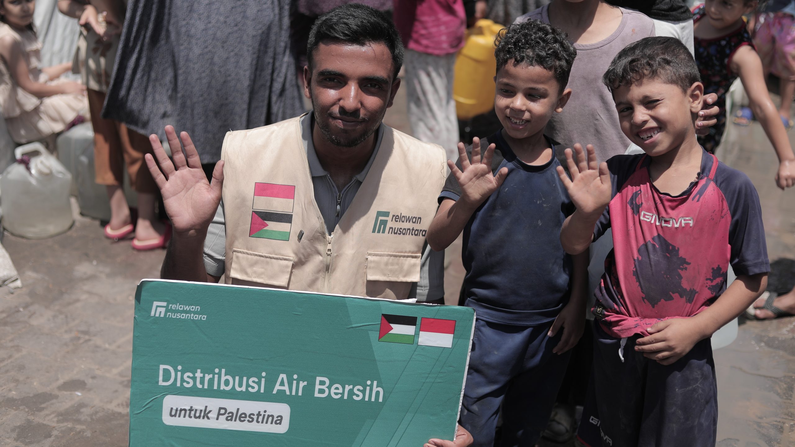 relawan-nusantara-dan-anak-anak-bantuan-air-bersih-gaza Relawan Nusantara bersama anak-anak Palestina membentangkan papan informasi bantuan air bersih di Gaza.
