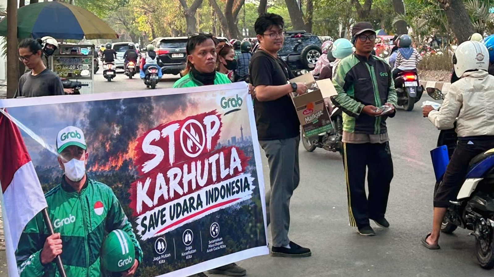 Relawan dan pengemudi ojol membentangkan spanduk imbauan pencegahan karhutla sambil membagikan biskuit serta masker kepada pengguna jalan di Makassar.