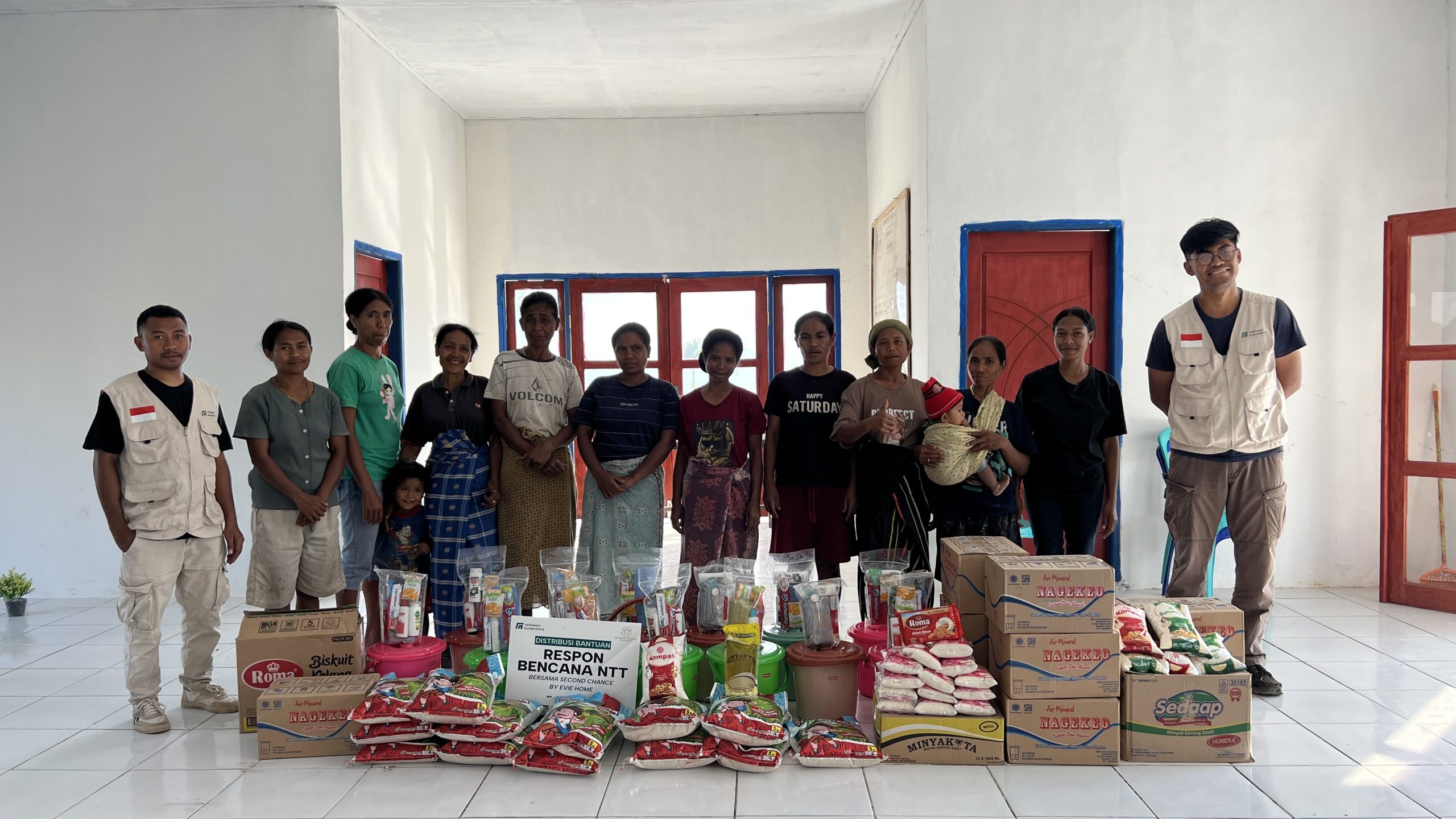 penyerahan-bantuan-sembako-hygiene-kit-second-chance-relawan-nusantara Tim Relawan Nusantara dan penerima manfaat berfoto bersama di balik tumpukan paket sembako, hygiene kit, dan air kemasan bantuan Second Chance by Evie Home.