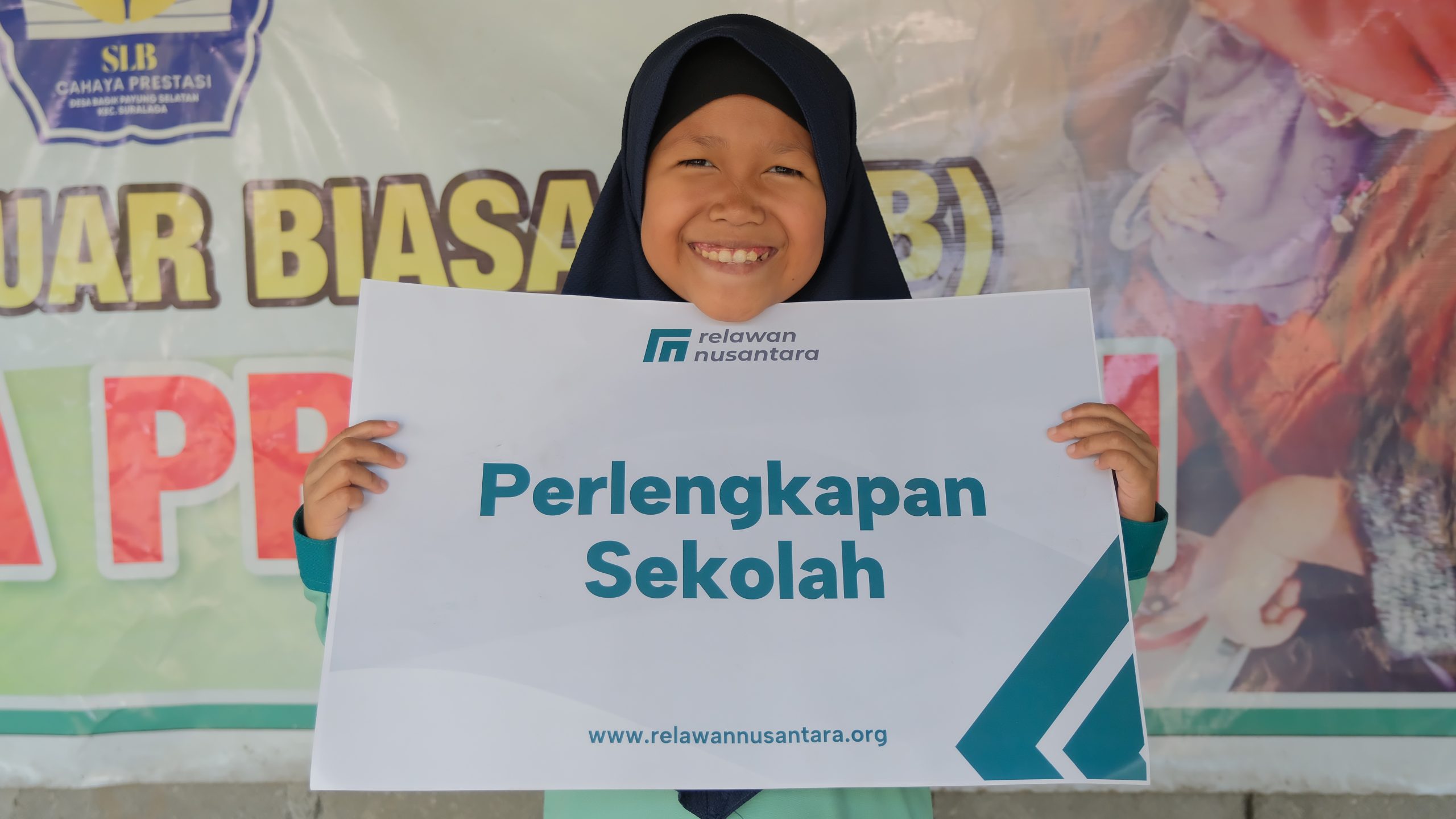 Siswa SLB Cahaya Prestasi memegang papan simbolis bantuan perlengkapan sekolah Relawan Nusantara.